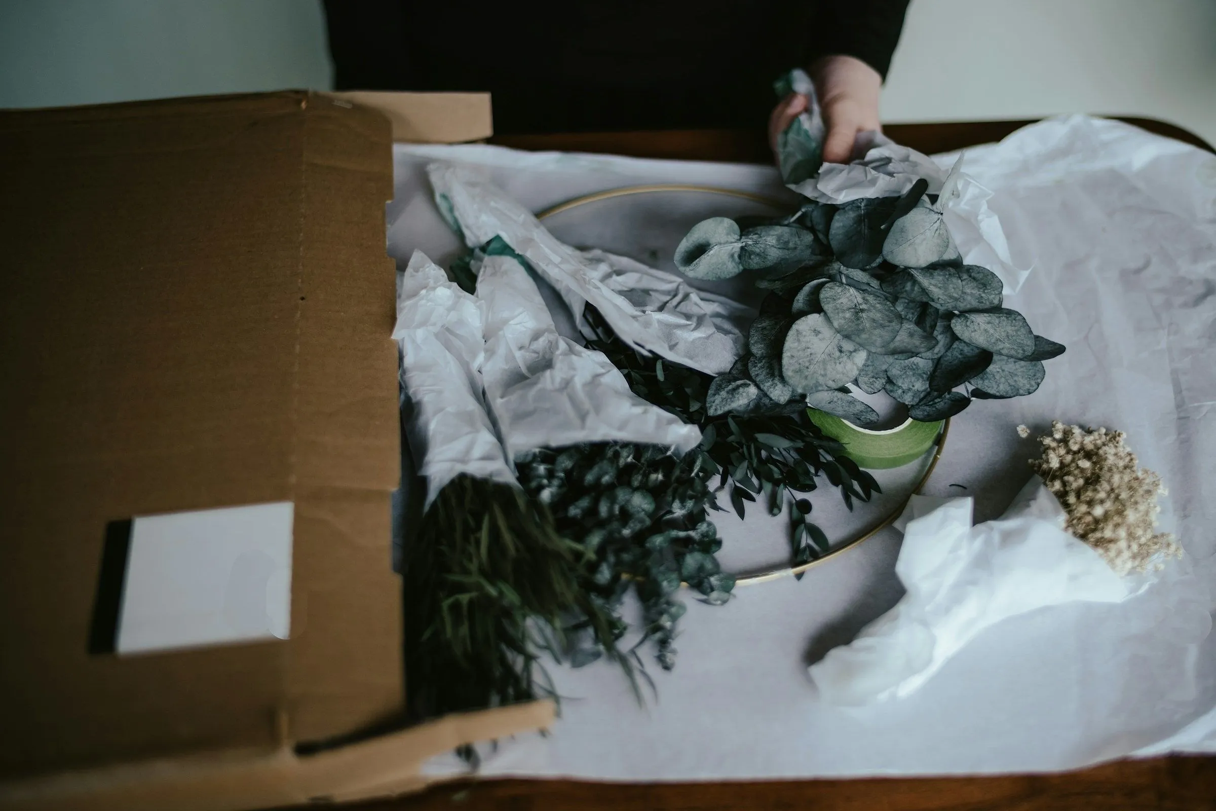 Hands placing tissue-wrapped greenery into a shipping box