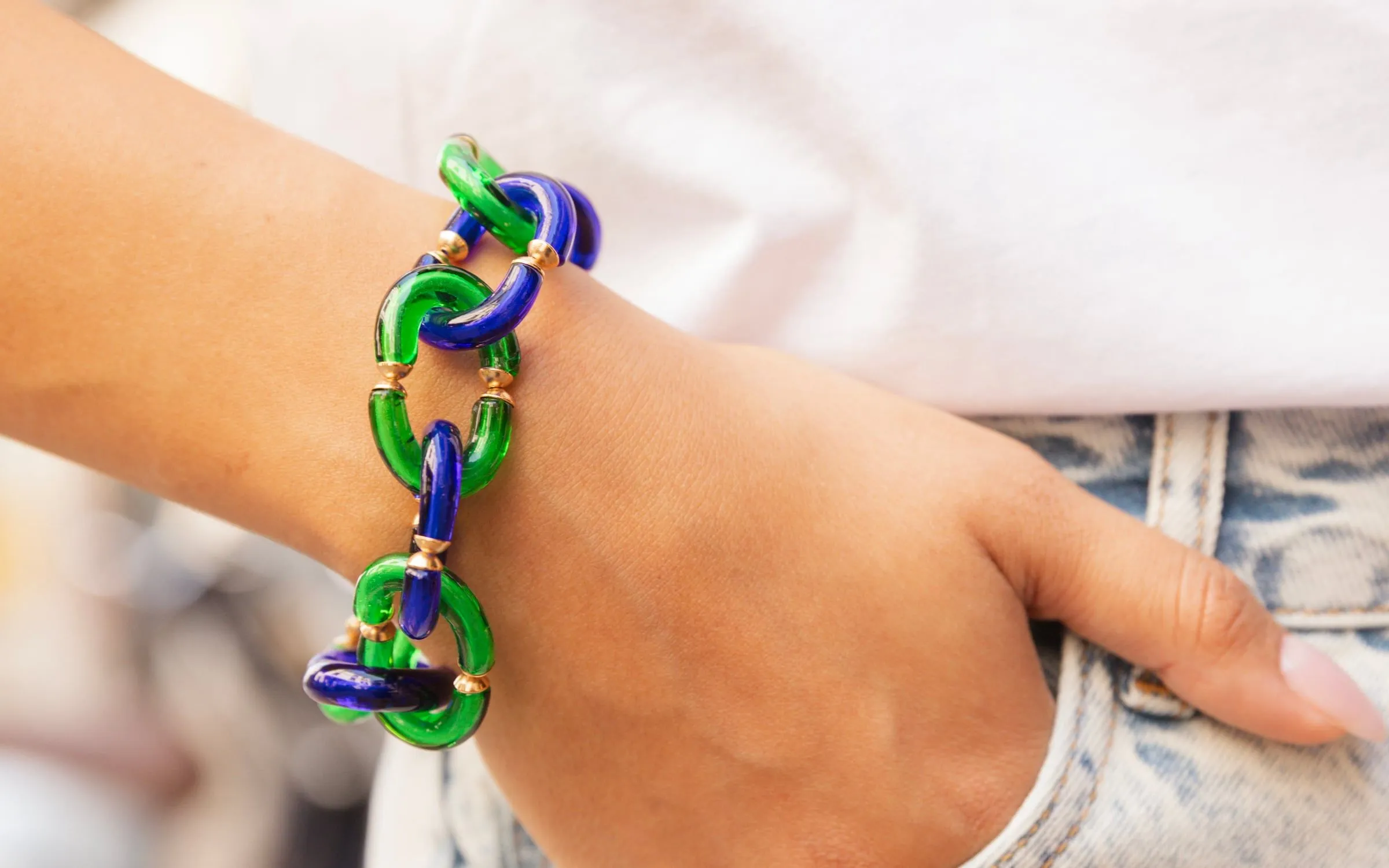 A green and cobalt Murano glass chain bracelet on a wrist, the hand resting in the pocket of pale jeans