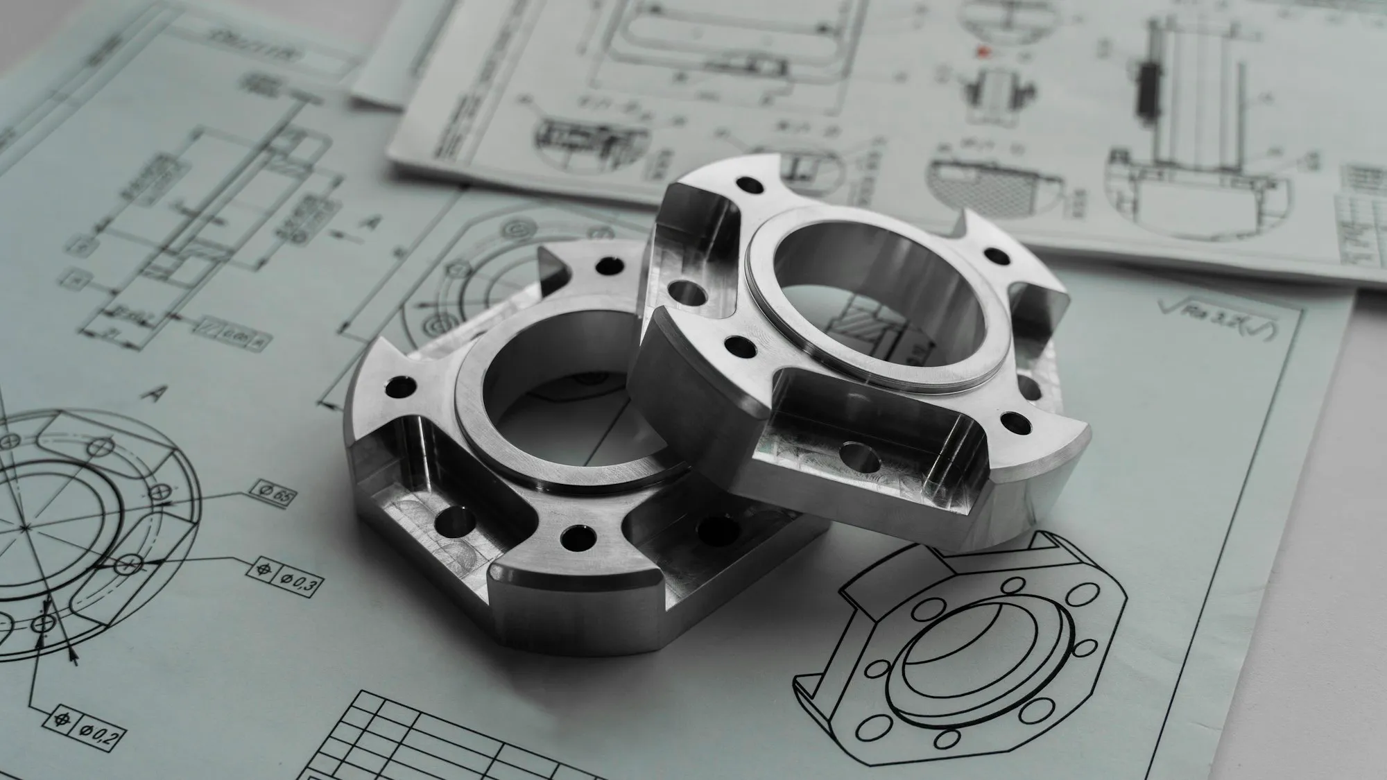 Teknik çizimlerin üzerinde iki işlenmiş metal parça
