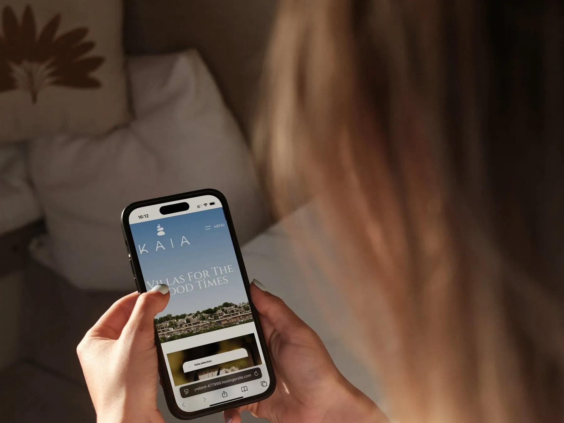A woman holding a phone open on the Kaia home page in a softly lit room