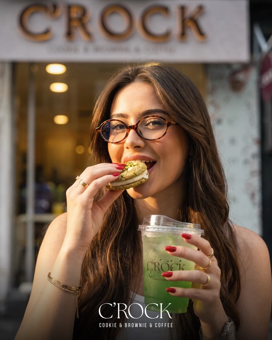 A woman in glasses biting a cookie outside the C'ROCK shop