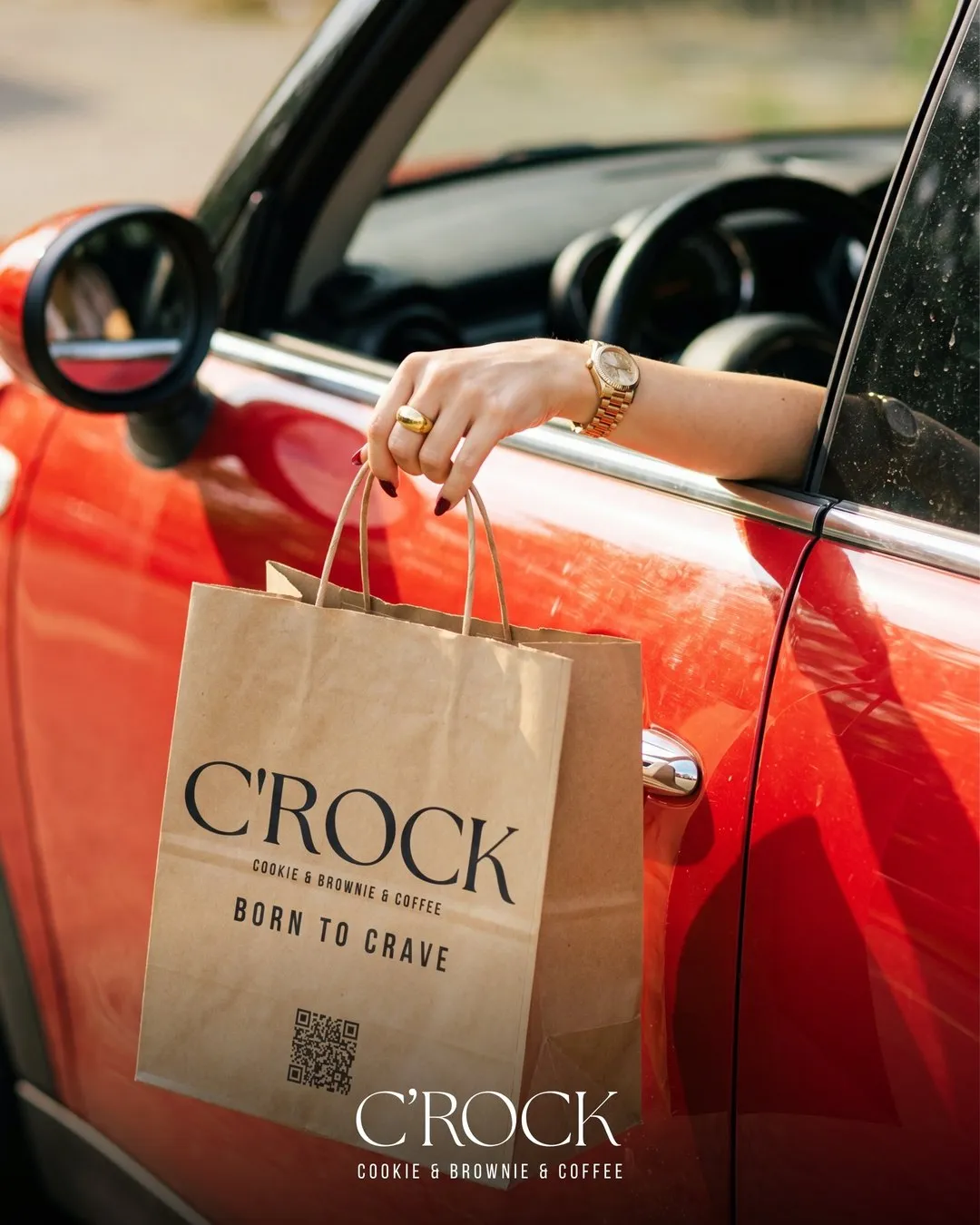 A C'ROCK paper bag held out of the window of a red car