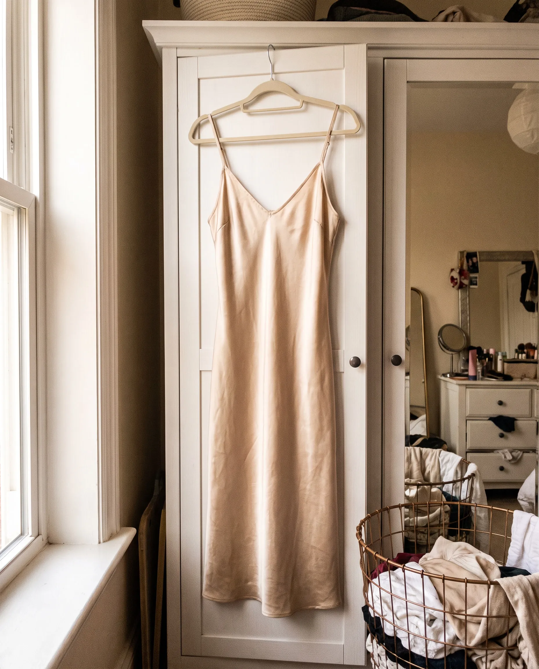 Ein champagnerfarbenes Slipdress aus Seide an einer Kleiderschranktür