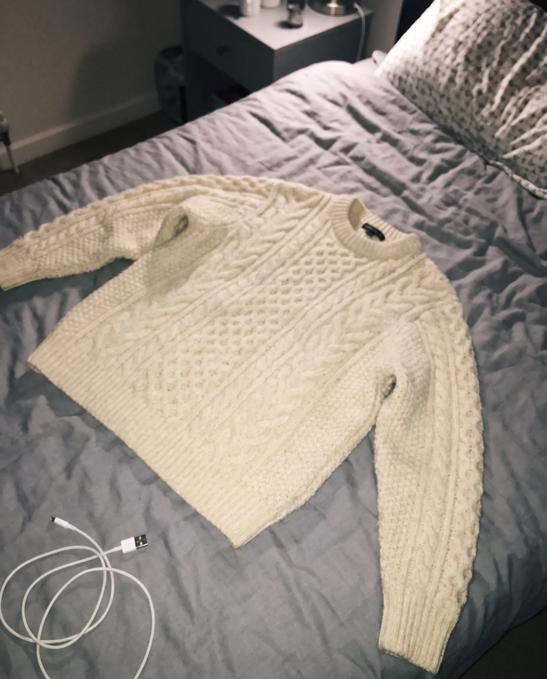 Ein cremefarbener Zopfstrickpullover, mit Blitz auf einem ungemachten Bett fotografiert